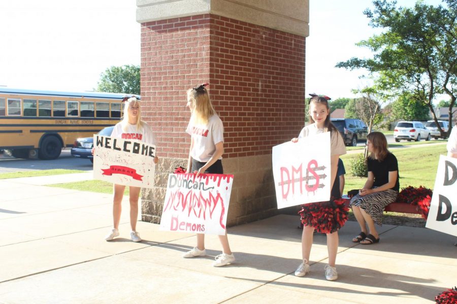 Eighth-grade cheerleaders Abby Carter, Sandra Billings and Serenity Stanley hold signs as fifth-grade buses roll up.