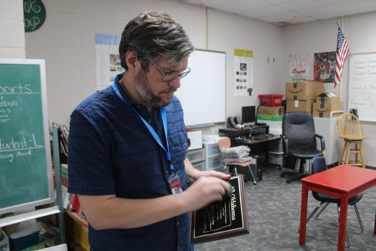 Derrick Miller, journalism teacher, rubs finger prints off the All-Oklahoma plaque the Demon Direct staff received Tuesday at Oklahoma Scholastic Media Day.