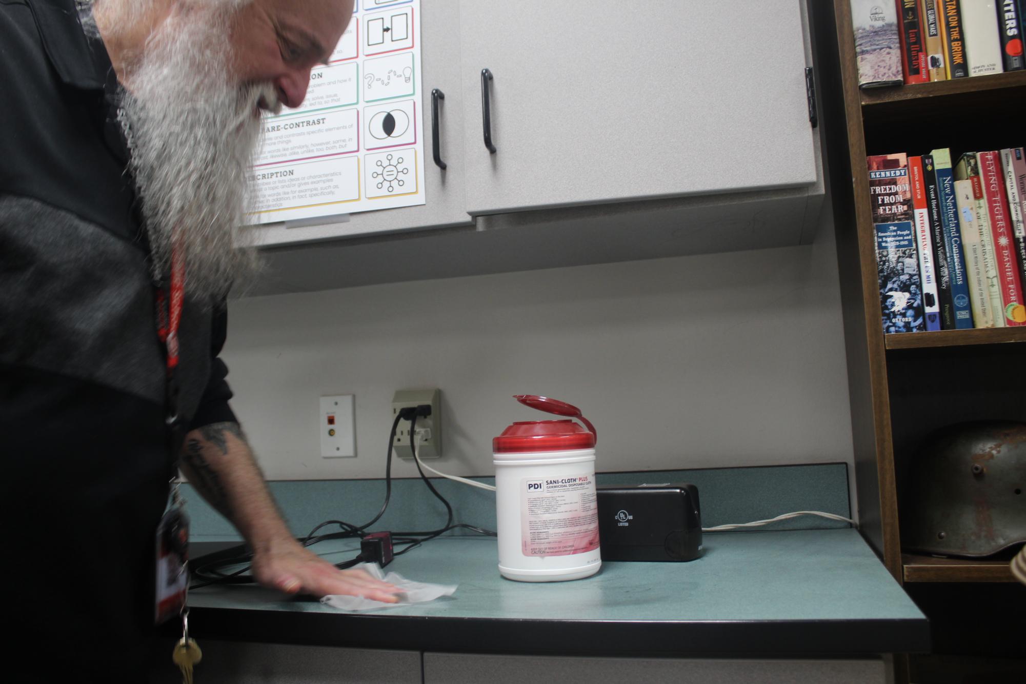 Social studies teacher Chuck Wagner wipes down the counter in his classroom.