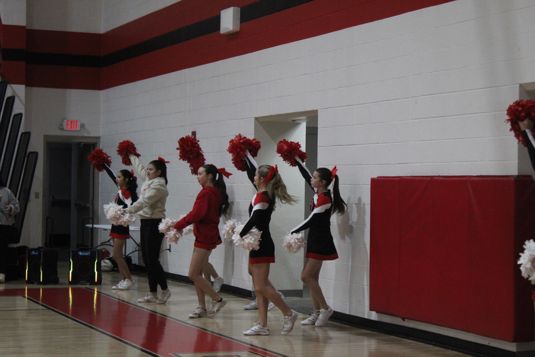 Cheerleaders perform on the side of a basketball game.