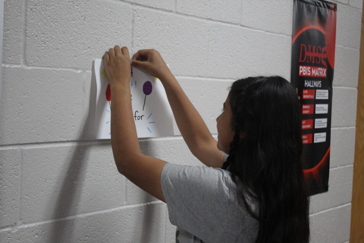 Yoselin Ontiveros hangs up a candidacy poster in the seventh-grade hallway. Student Council elections are Friday.