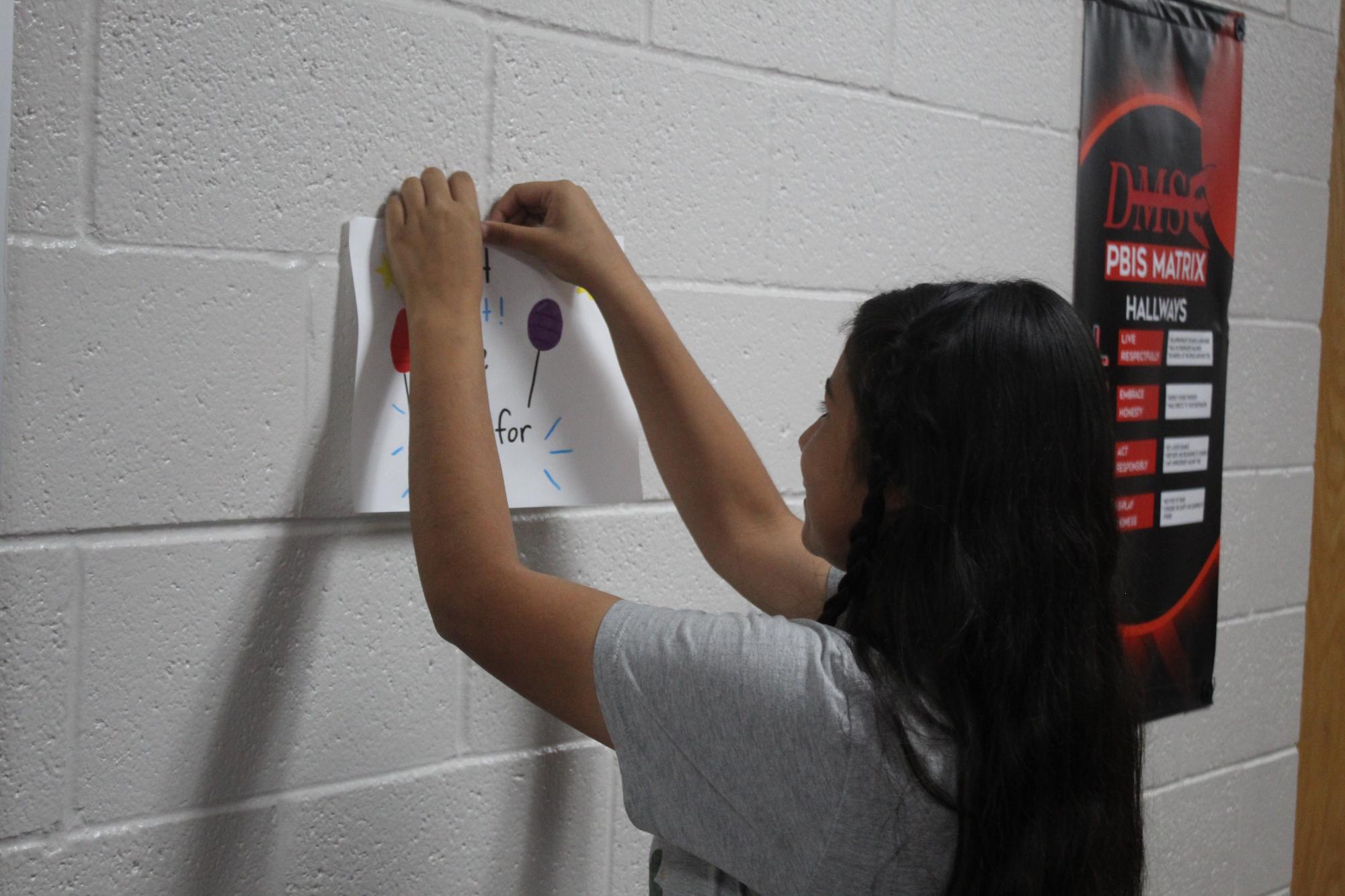 Yoselin Ontiveros hangs up a candidacy poster in the seventh-grade hallway. Student Council elections are Friday.